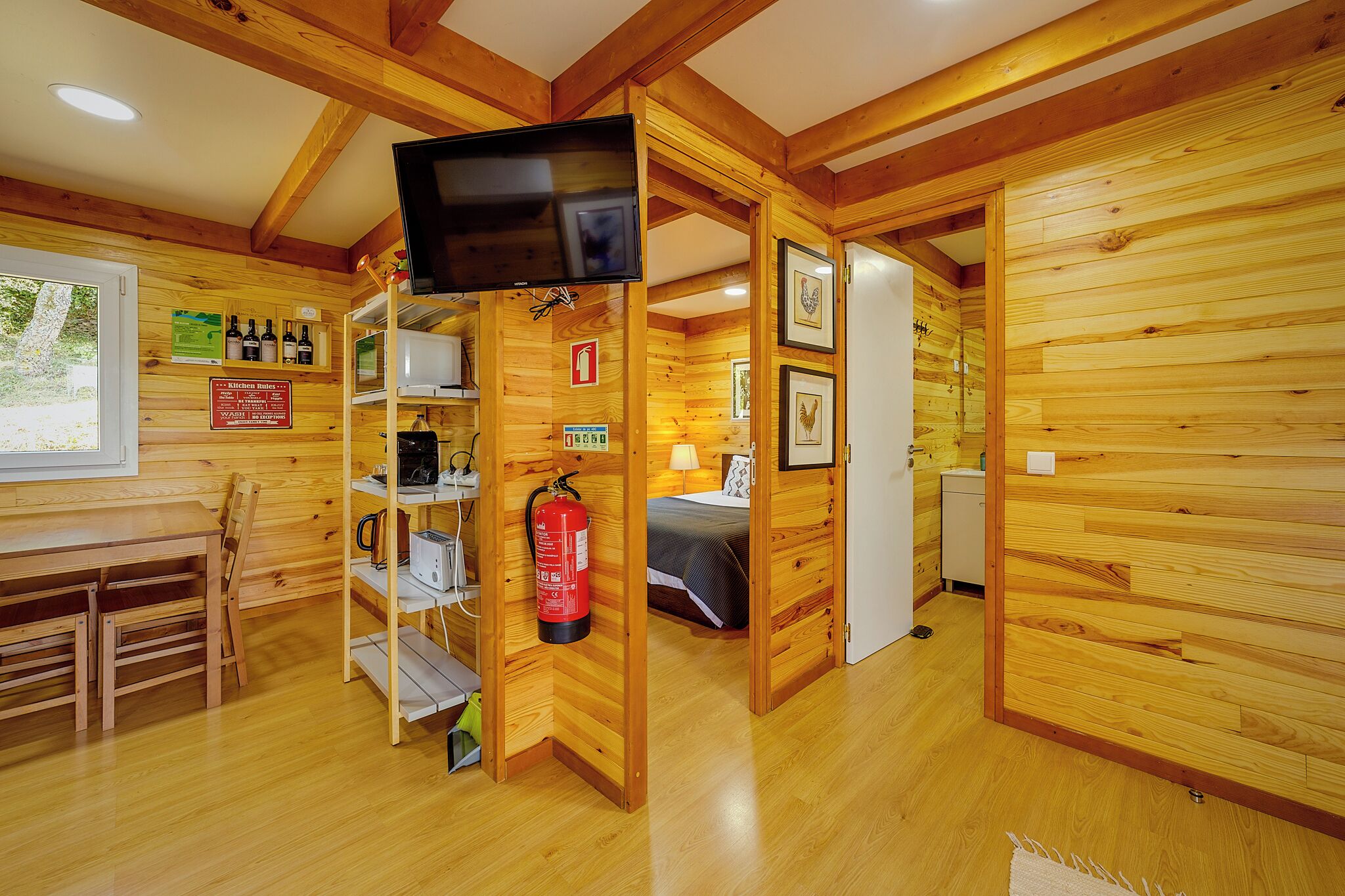 Ein Holzblockbau-Innenraum mit Küchenzeile, einem Bett und einem an einer Wandregal montierten Fernseher.