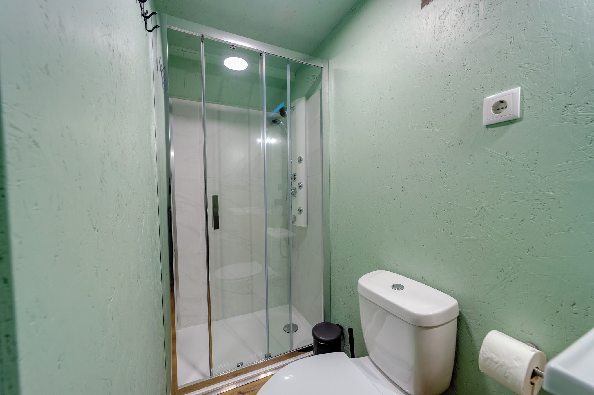 A bathroom with a glass-enclosed shower, a toilet, and a wall-mounted light fixture.