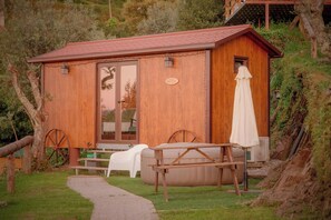Una cabaña de madera con puerta de vidrio, un banco, una mesa y un paraguas.
