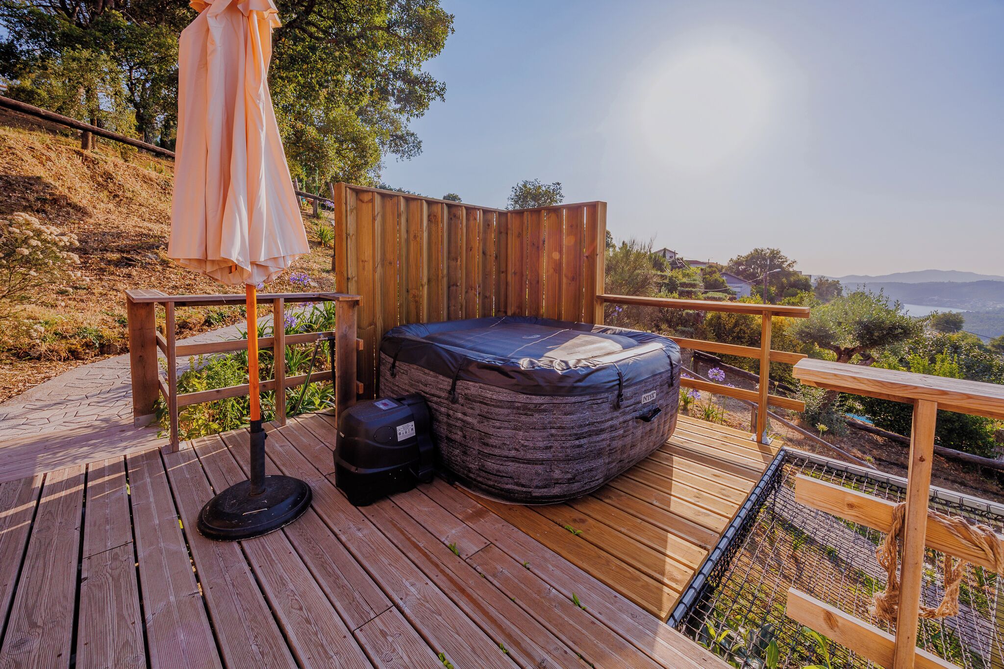 A wooden deck with a blue outdoor bed, a portable grill, and an umbrella.