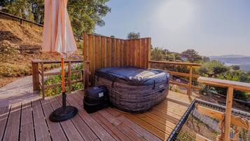 A wooden deck with a blue outdoor bed, a portable grill, and an umbrella.