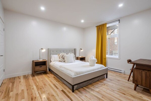 A bedroom with a bed, bedside tables, a desk, and a window with curtains.