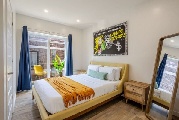 A modern hotel room with a bed, a nightstand, a mirror, and a large window with curtains.