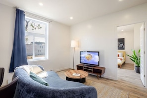 A modern living room with a sofa, a coffee table, a flat-screen TV, and a view of the outside.