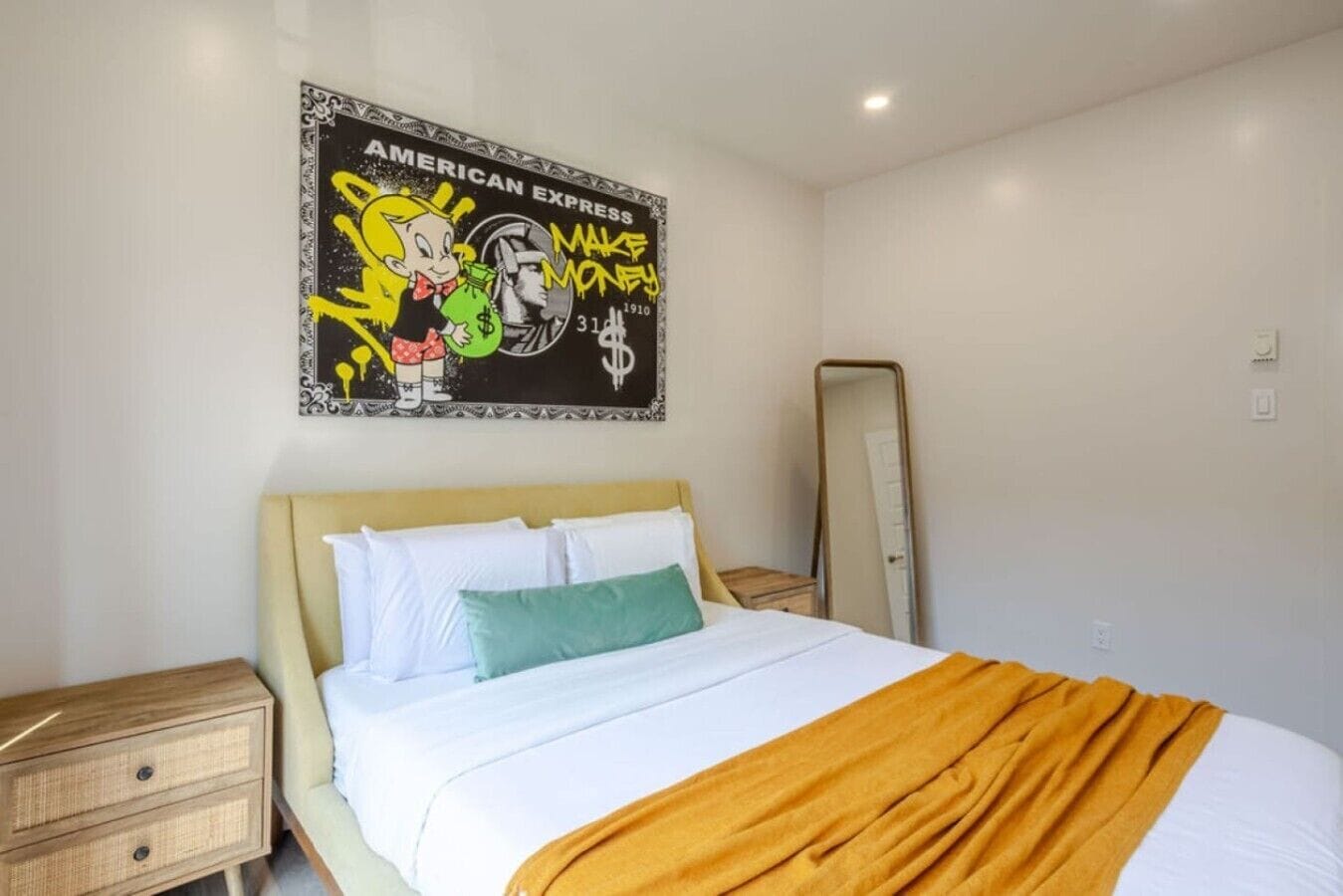 Quarto de hotel com cama, mesa de cabeceira, espelho e um quadro na parede.