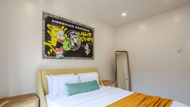 Quarto de hotel com cama, mesa de cabeceira, espelho e um quadro na parede.