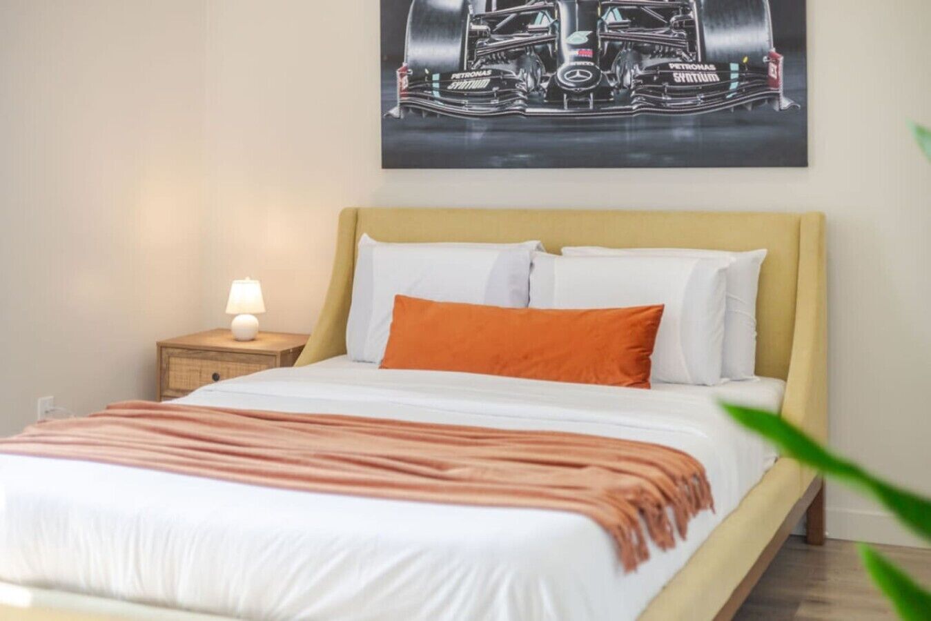 A neatly made bed with white and orange bedding, a bedside lamp, and a wall-mounted artwork.