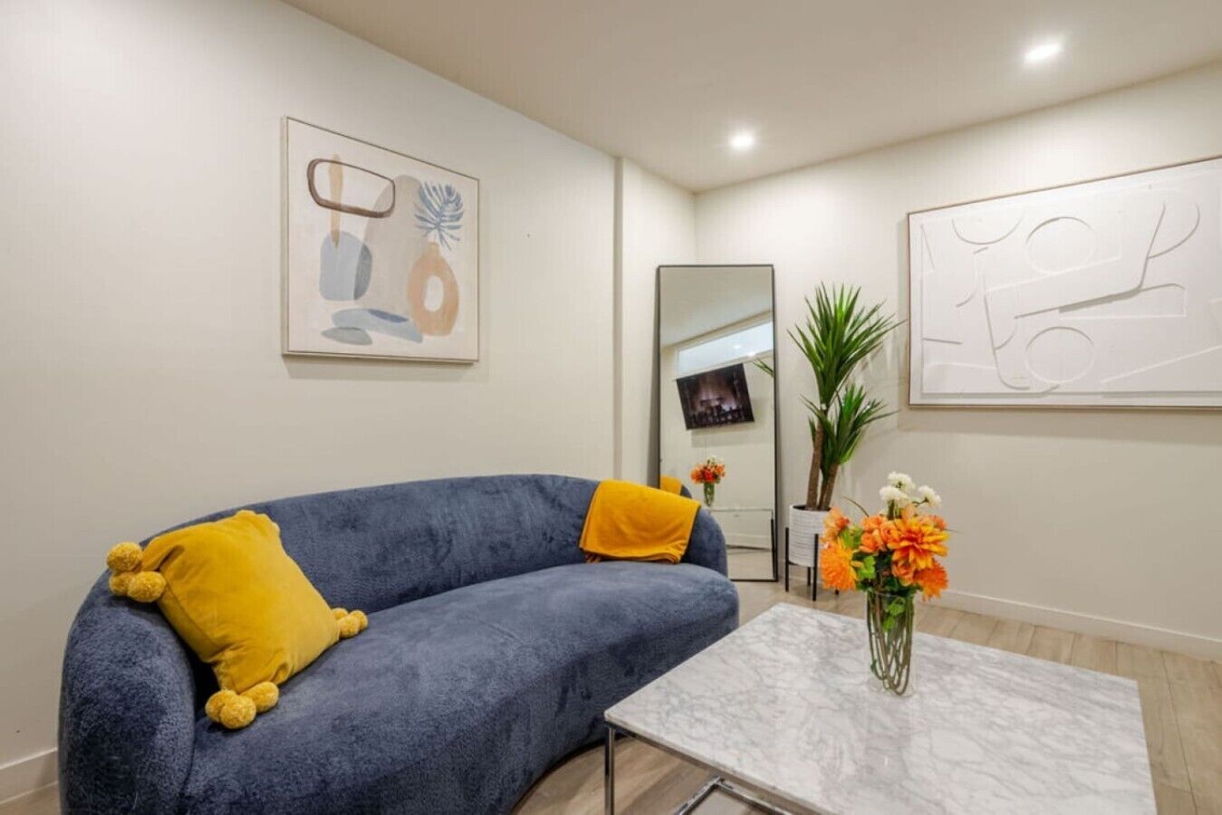 A modern living room with a blue sofa, a yellow pillow, a marble coffee table, and a vase of flowers.