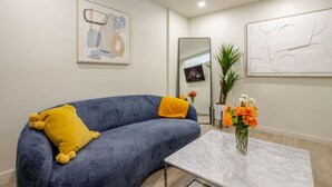 Uma sala de estar moderna com um sofá azul, um travesseiro amarelo, uma mesa de centro de mármore e um vaso com flores.