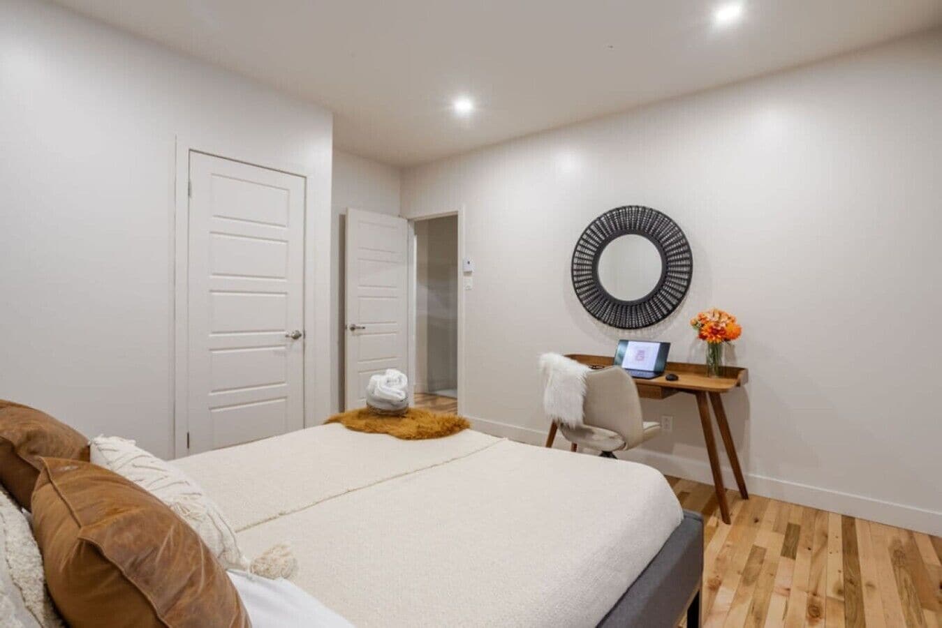 Un dormitorio con una cama, un escritorio con una computadora portátil, un espejo y una puerta.