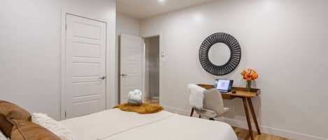 Un dormitorio con una cama, un escritorio con una computadora portátil, un espejo y una puerta.
