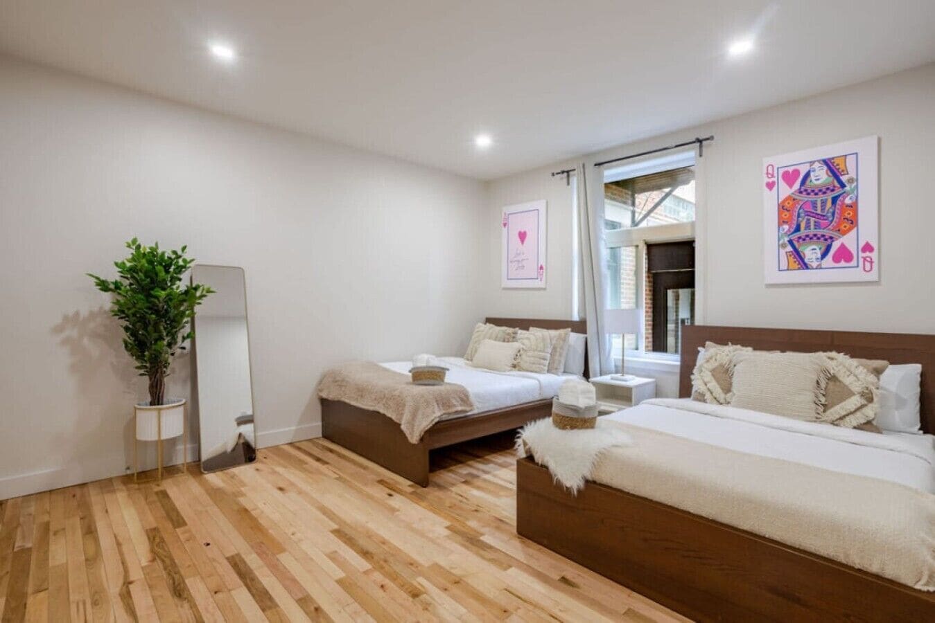 A bedroom with two beds, a mirror, a potted plant, and artwork on the walls.