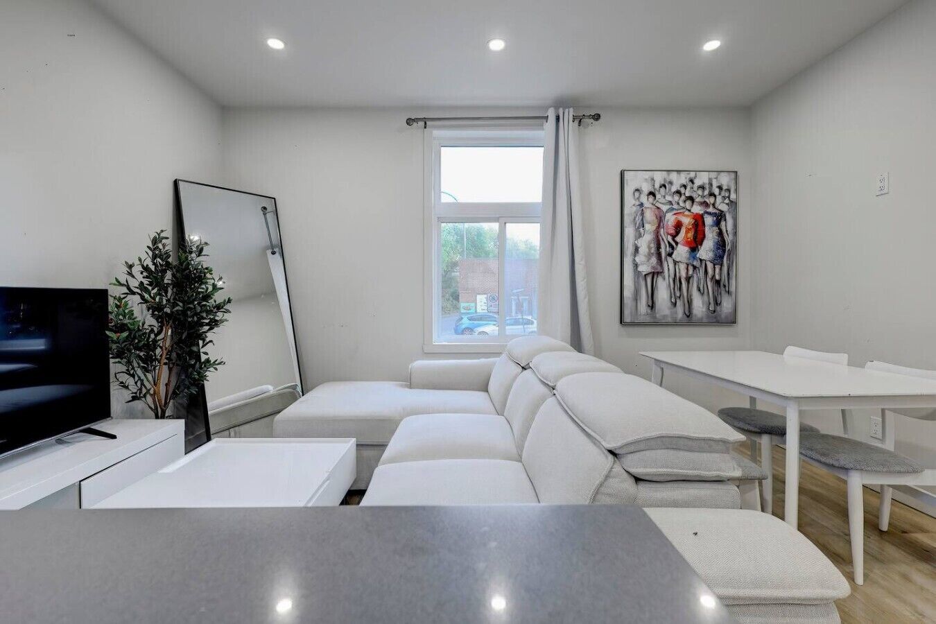 A modern living room with a sofa, a TV, a dining table, and a painting on the wall.