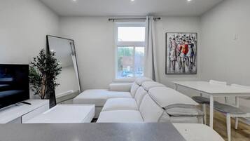 A modern living room with a sofa, a TV, a dining table, and a painting on the wall.