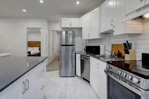 A modern kitchen with stainless steel appliances, white cabinetry, and a marble floor. - Cozy & Bright | Prime Location (Montreal)