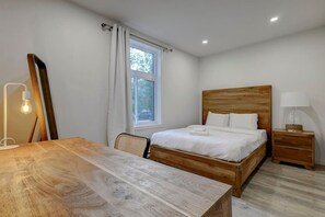 Un dormitorio con cama de madera, una mesita de noche, una silla, un escritorio, una lámpara y una ventana con cortinas.