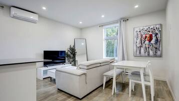 A modern living room with a flat-screen TV, a sofa, a dining table, and a window with curtains.