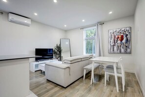 Una sala de estar moderna con un televisor de pantalla plana, un sofá, una mesa de comedor y una ventana con cortinas.