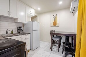 A compact kitchen with white cabinets, a refrigerator, a stove, and a dining area with a table and chairs. - Spacious Retreat in Montréal (Montreal)