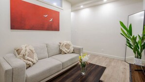 Ein modernes Wohnzimmer mit einem beigen Sofa, einem roten abstrakten Gemälde, einem Holztisch und einer Topfpflanze.
