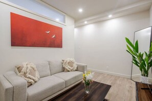Una sala de estar moderna con un sofá beige, un cuadro abstracto rojo, una mesa de centro de madera y una planta en maceta.