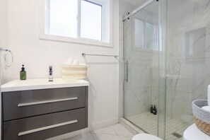Un baño moderno con cabina de ducha de vidrio, tocador con espejo y ventana sobre el lavabo.