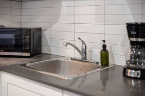 Una cocina con un lavamanos de acero inoxidable, un microondas negro y una botella verde.