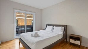 Ein Schlafzimmer mit einem Bett, einem Nachttisch, einem Fenster und Blick auf ein Backsteingebäude.
