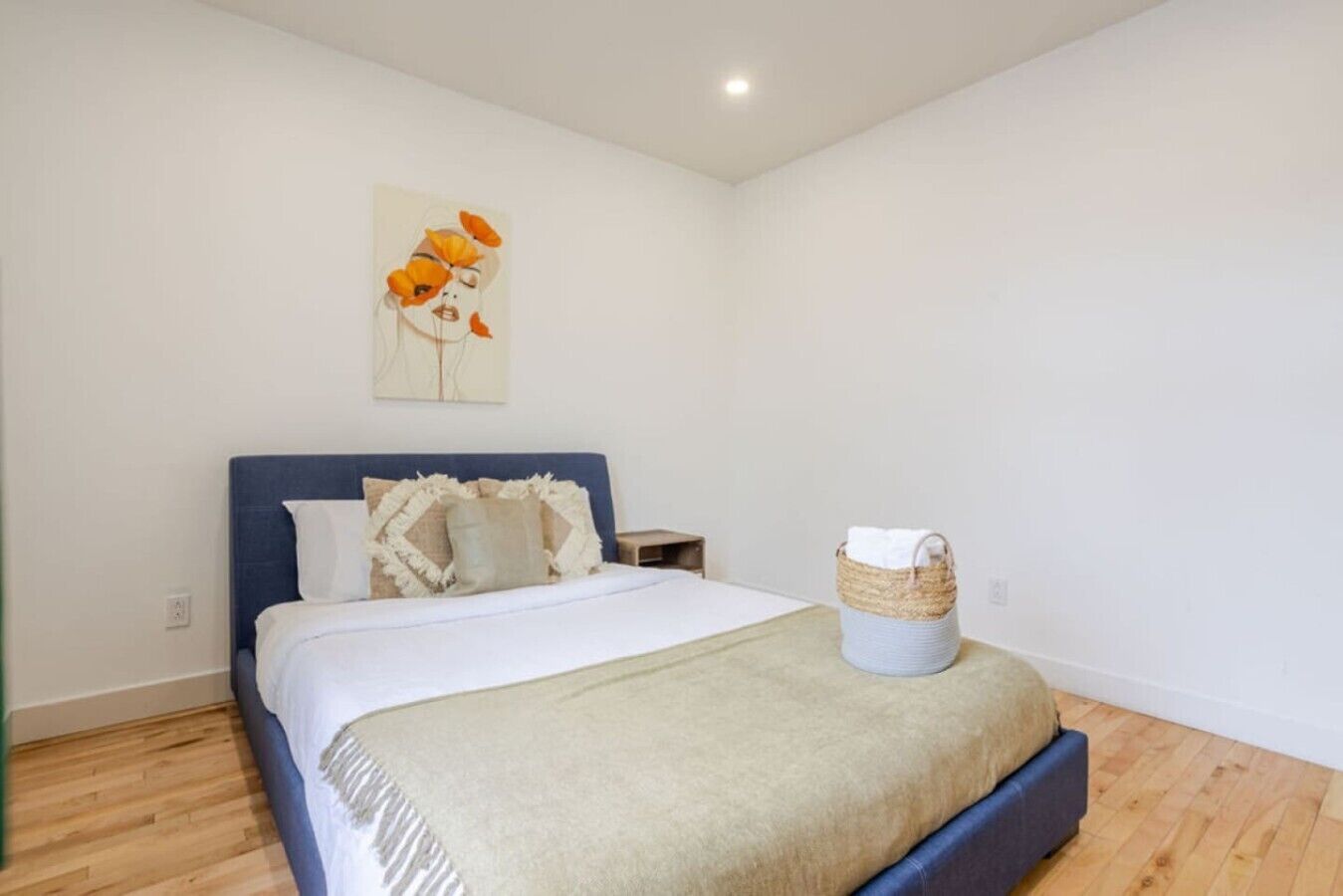 A bedroom with a bed, a headboard, a wall art piece, a bedside table, and a basket.