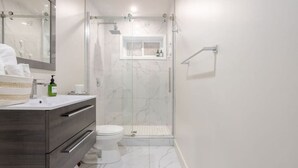 A modern bathroom with a glass-enclosed shower, a white toilet, and a vanity with a mirror.
