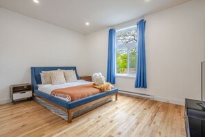 Ein Schlafzimmer mit Bett, Nachttisch, Fenster mit Vorhängen und Blick ins Grüne.