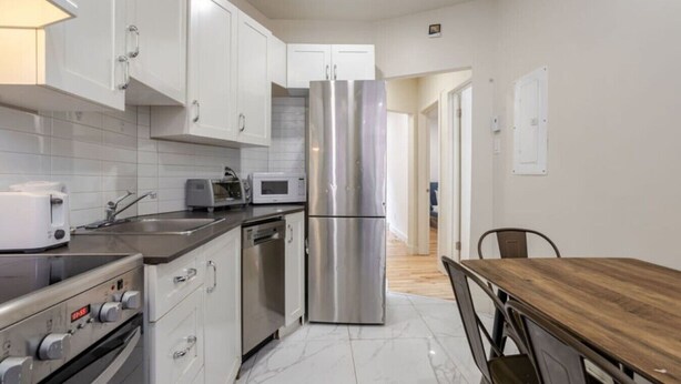 A modern kitchen with stainless steel appliances, white cabinetry, and a wooden dining table.