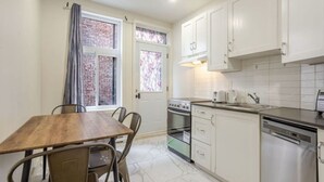 A compact kitchen with white cabinets, a wooden dining table, and a window with a view of a brick wall.