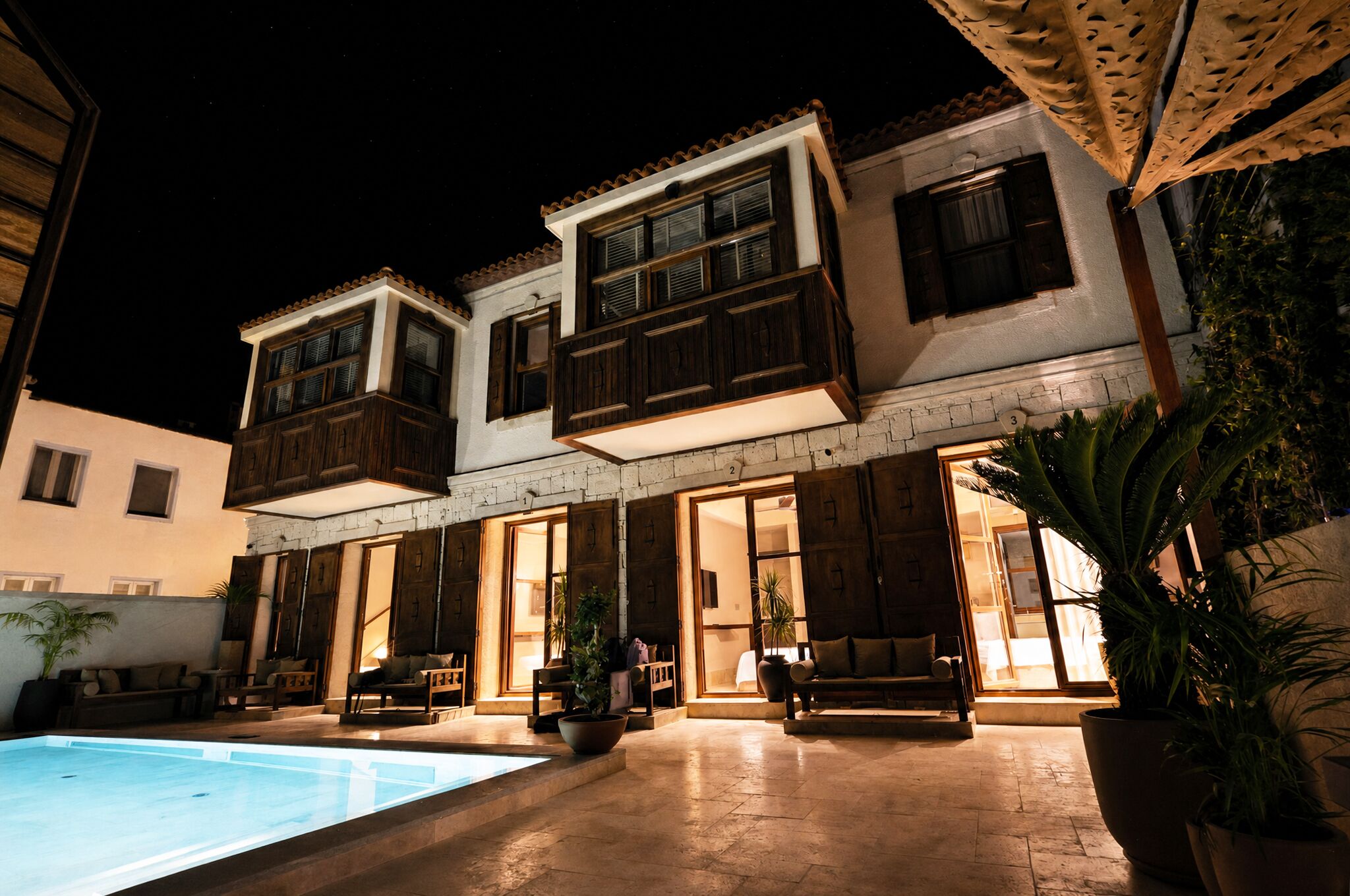 A two-story building with a swimming pool, wooden balconies, and potted plants.