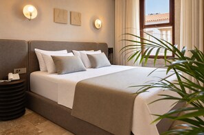 Een opgemaakt bed met hoofdeinde, nachtkastje met telefoon en wandlampen.