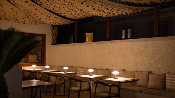 Un restaurante con mesas y sillas, techo estampado y vista a la calle.