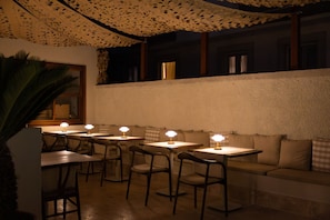 Um restaurante com mesas, cadeiras, teto estampado e vista para a rua.