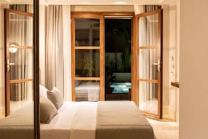 Quarto com cama, cortinas e vista através de uma porta de vidro.