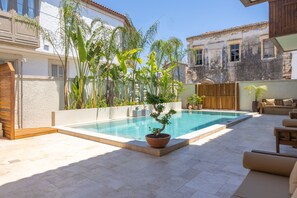 A swimming pool with a potted bonsai tree, outdoor furniture, and a building with a white facade and wooden balcony. - House Sola Alaçatı (Cesme)