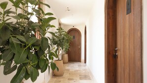 Un pasillo con una planta en maceta, una puerta de madera y suelo de baldosas.
