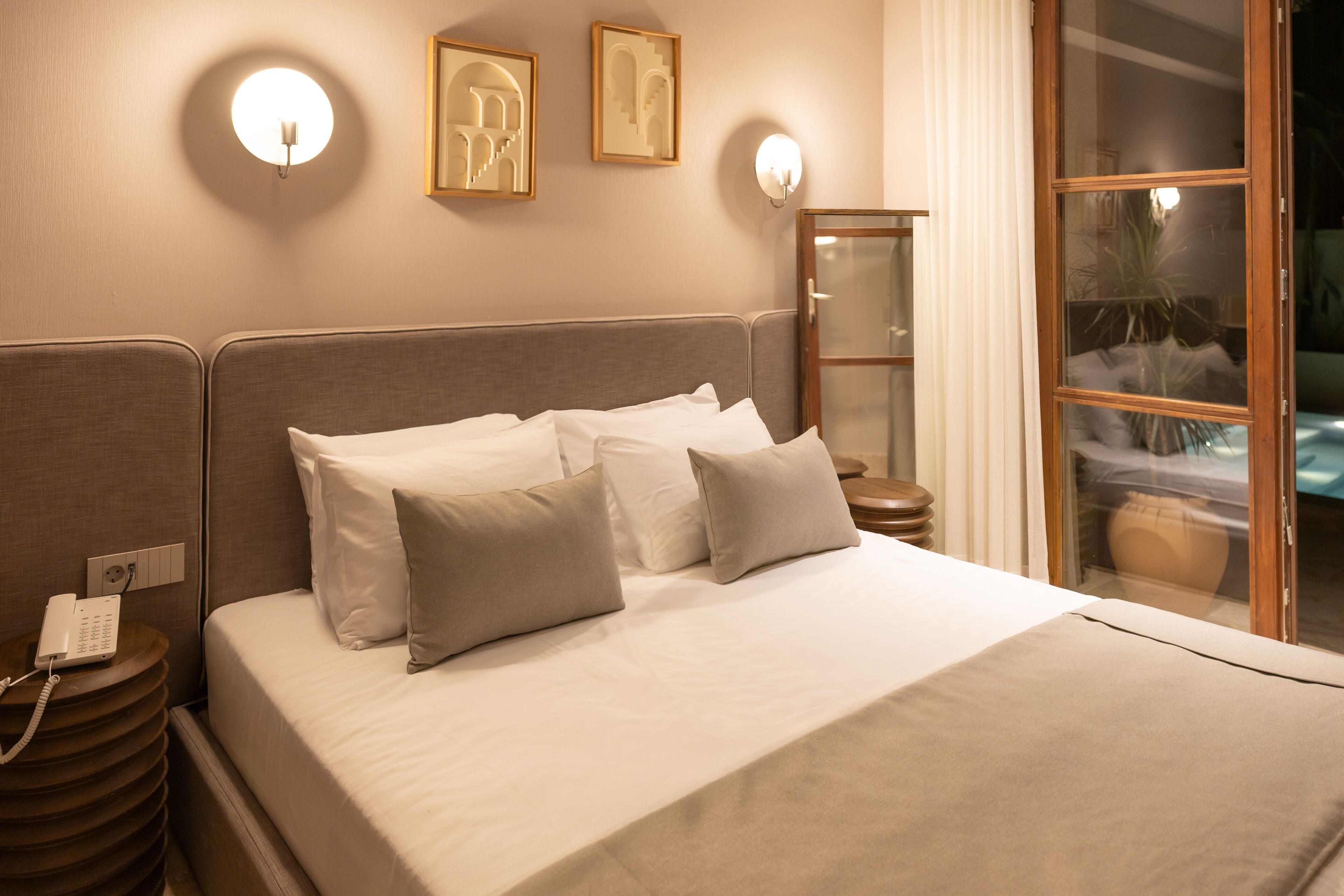 Una habitación de hotel con cama, mesita de noche con teléfono, apliques de pared y cuadro enmarcado.