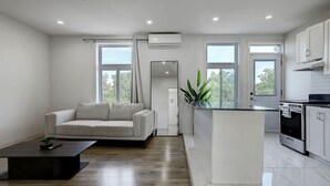 A modern kitchen with a central island, a sofa, and a coffee table in a bright living area with large windows.
