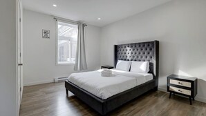 Ein modernes Schlafzimmer mit einem großen Bett, einem Nachttisch, einem Fenster mit Vorhängen und einem Schild an der Wand.