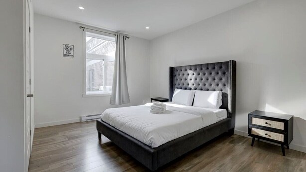 A modern bedroom with a large bed, a nightstand, a window with curtains, and a sign on the wall.