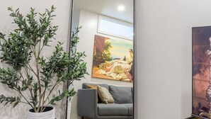 A room with a large mirror, a grey sofa, a painting, and a potted plant.