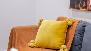 A blue sofa with a yellow pillow and orange throw blanket.