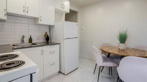 A modern kitchen with white cabinets, a refrigerator, a stove, and a dining area with a table and chairs.