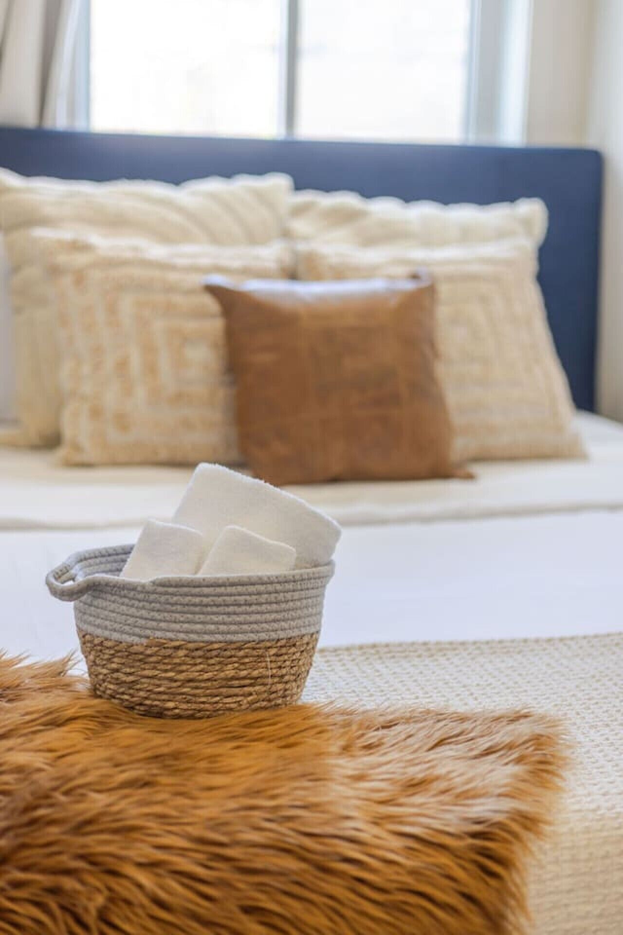 A bed with pillows, a basket with tissues, and a fur-like cushion.