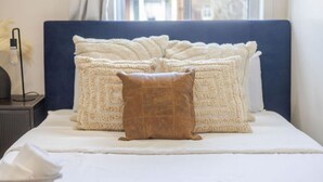 A bed with a blue headboard, white bedding, and two decorative pillows.