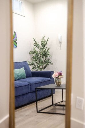 Ein Zimmer mit einem blauen Sofa, einem kleinen Tisch, einer Topfpflanze und einem an der Wand montierten Telefon.